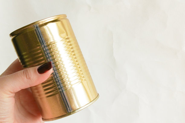 一只女性的手在白色背景上握着一个金色罐头，右侧留有文字位置。长保质期的罐装食品。罐头食品的宣传照片。图片下载