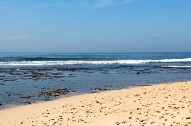 阳光明媚的日子里，海浪拍打着沙滩。水边的沙子上留有脚印。自然海景，壁纸，照片。图片下载