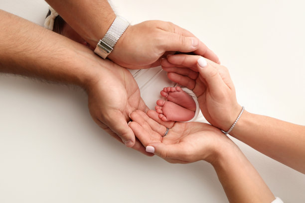 父母的手掌。一位父亲和母亲在白色背景上抱着裹着白色毛毯的新生儿的脚。新生儿的脚在父母的手中。脚、脚跟和脚趾的照片。图片下载