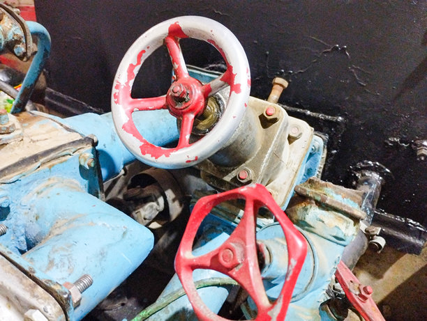 金属阀门和管道的特写。可以看到两个带有红色和白色元素的阀门，以及涂有蓝色漆的金属管道。照片传达了工业设备的细节和质感。图片下载