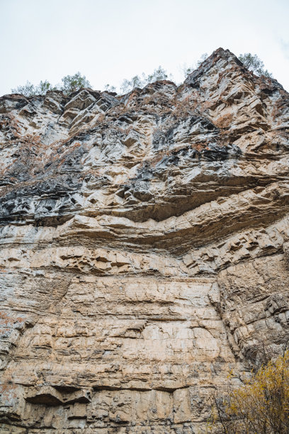 这张图片展示了一个粗犷的岩石悬崖的细致特写，悬崖高耸入云，背景中可见壮丽的山脉，增强了整体的风景效果。图片下载