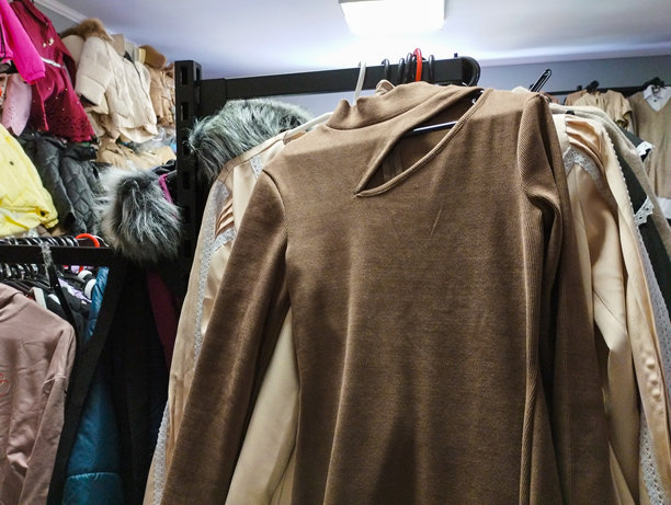 这张照片展示了商店里挂在衣架上的女性服装特写。焦点是一件棕色长袖连衣裙，胸部有开口设计。图片下载