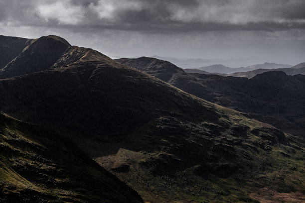 这张照片描绘了一系列山脉。最近的山脉显示出岩石、深棕色和黑色的坡度。图片下载