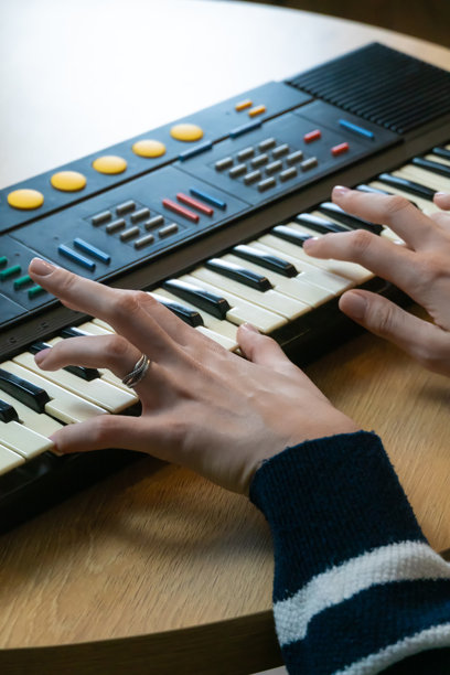 女性手部特写，正在演奏复古合成器键盘，在家庭工作室中创作电子音乐，展现音乐创意与热情。竖版照片图片下载