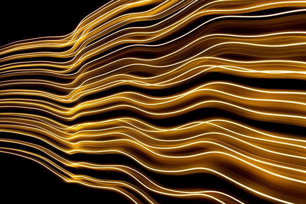 一张长时间曝光的照片，展示了在黑色背景下，五彩斑斓的金色光线以平行线条旋转延伸至远方。图片下载