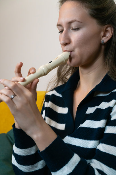 年轻女性音乐家坐在黄色沙发上演奏直笛，穿着条纹毛衣，正在练习她的乐器。竖版照片图片下载