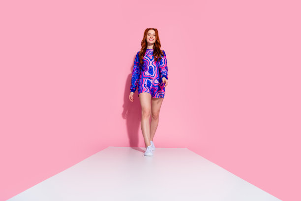 年轻女士穿着时尚的蓝色印花服装，在粉色背景下走在白色小路上，拍摄的全身照片。图片下载