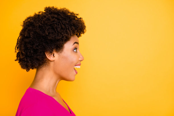 侧面照片，卷发时尚的惊讶迷人女友，欣赏地看着某样东西，背景为鲜艳的黄色。图片下载