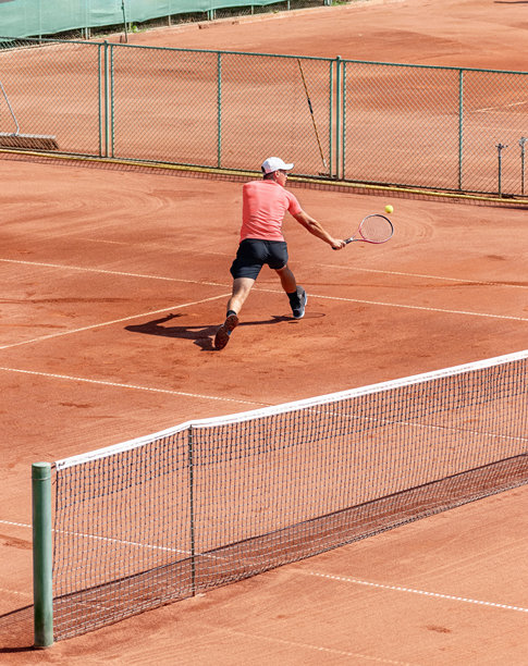 年轻男性网球运动员在比赛或训练中用网球拍击球的动态照片。年轻运动员专注于在红色泥土场地上的比赛。积极的生活方式，体育活动，竞争。图片下载