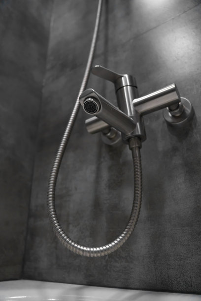 现代浴室中，灰色瓷砖墙上安装的不锈钢淋浴水龙头特写，配有灵活的金属软管，展示了现代管道配件。竖版照片图片下载