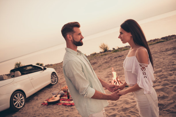 穿着休闲服的情侣在海滩上牵手，靠近汽车，享受旅行时光的照片肖像图片下载