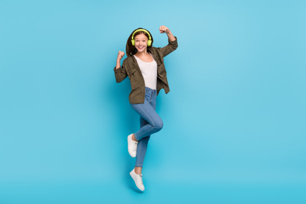 全身照片，快乐的休闲装女孩无忧无虑地跳跃，举起拳头，庆祝幸运的目标，背景为蓝色。图片下载