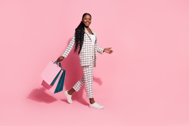 年轻时尚女孩在粉色背景下走在购物中心，享受折扣的全身侧面照片图片下载