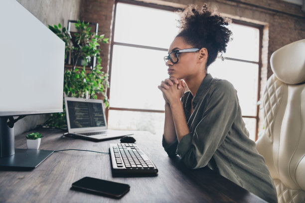 专注的女性极客侧面照片，坐在桌子前，盯着屏幕，进行头脑风暴，支持服务器网站，工作场所的工作站。图片下载