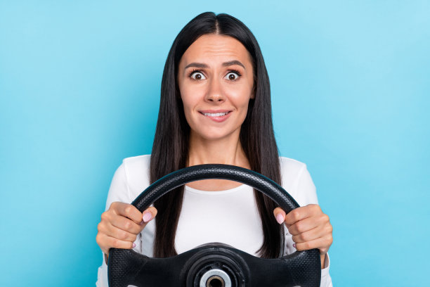 年轻可爱的女人在蓝色背景下咬着嘴唇，害怕快速驾驶汽车，度假时的照片图片下载