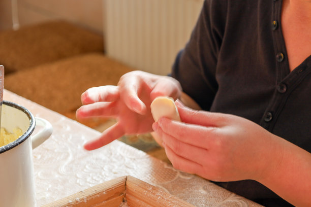 这张照片展示了一位女性的手在制作饺子（瓦伦基）的特写。她手中拿着一块面团，正在塑形。图片下载