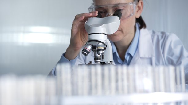 穿着实验室外套和防护眼镜的女科学家正在现代实验室中使用显微镜。低调照明照片。科学与医学图片下载