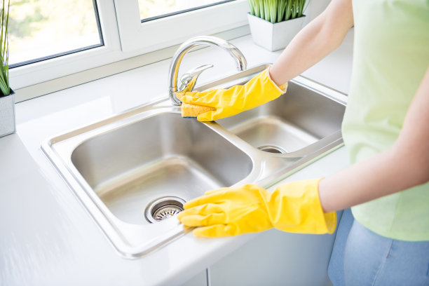 女士戴着橡胶手套用海绵擦拭厨房水槽的特写照片，阳光明媚的室内环境图片下载