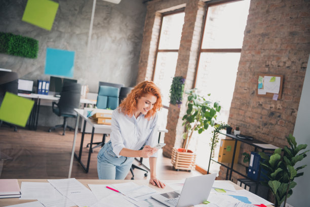 成功的年轻女性商务人士在现代阁楼办公室内使用智能手机和笔记本电脑的照片图片下载