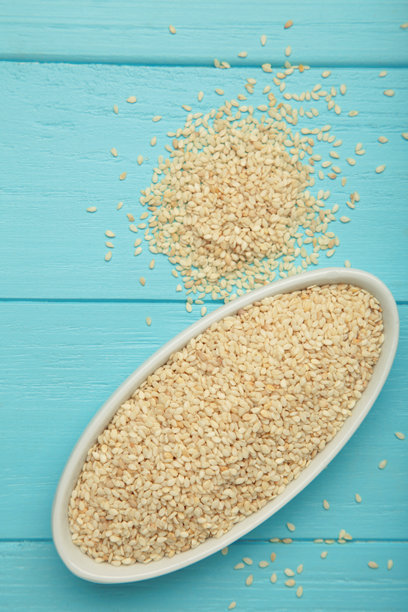 蓝色背景上白色碗中的生芝麻。竖版照片图片下载