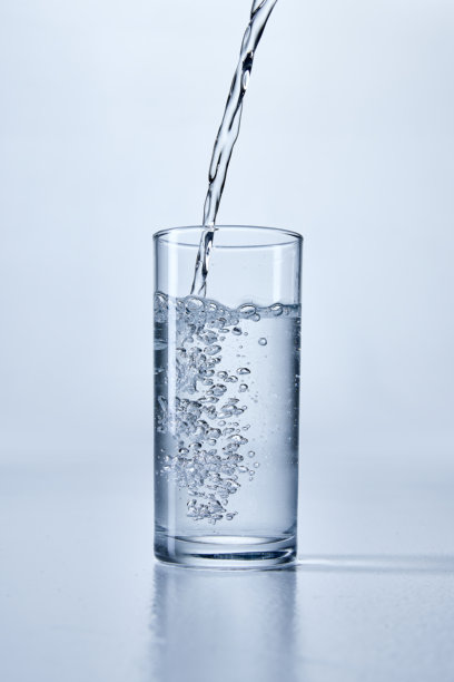 透明水被倒入一个清晰的圆柱形玻璃杯中，特写照片，展示了气泡和水花，背景柔和。样机。图片下载