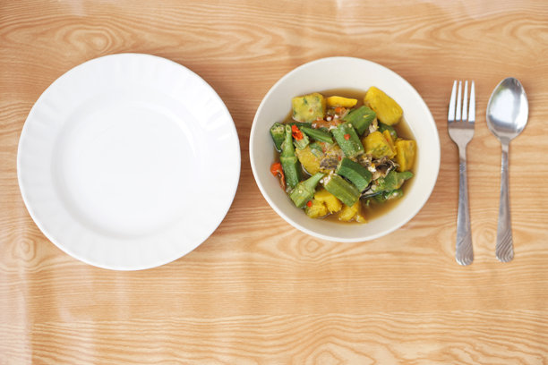 碗里装着混合有机秋葵、南瓜和泰国草药成分的咖喱。空盘子、勺子和叉子。概念：当地食物富含营养。健康饮食。高纤维和维生素。俯视拍摄的照片。图片下载