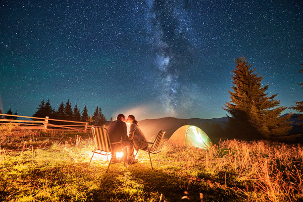 一对登山者在营火旁亲吻，坐在椅子上，仰望壮丽的星空和银河。图片下载