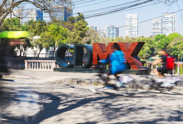 这张照片捕捉了墨西哥城充满活力的街景，特色的CDMX标志、骑行者在运动，以及被绿植环绕的现代建筑。图片下载