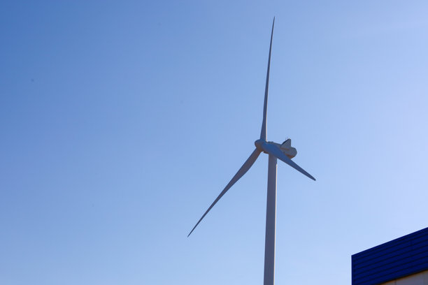 这张照片展示了一座风力涡轮机与晴朗的蓝天相映衬。涡轮机垂直放置，叶片朝不同方向延伸，形成了一个动感的图案。图片下载