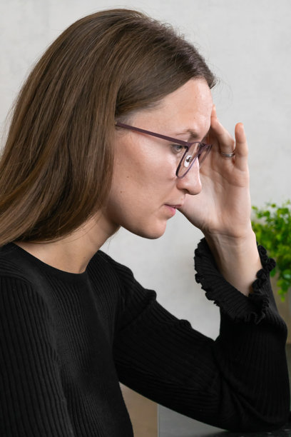 年轻女商人戴着眼镜，手触额头，因强烈的偏头痛而感到疲惫和精疲力竭，正在办公室工作。竖版照片图片下载