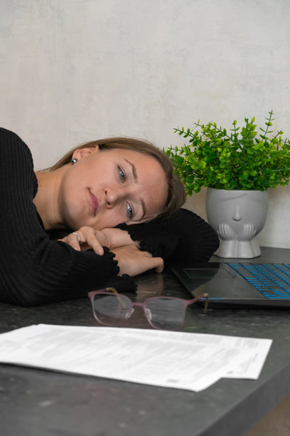 年轻女性趴在桌子上，头靠在桌面上，疲惫的自由职业者在辛勤工作后休息，桌上有文件和眼镜。竖版照片图片下载