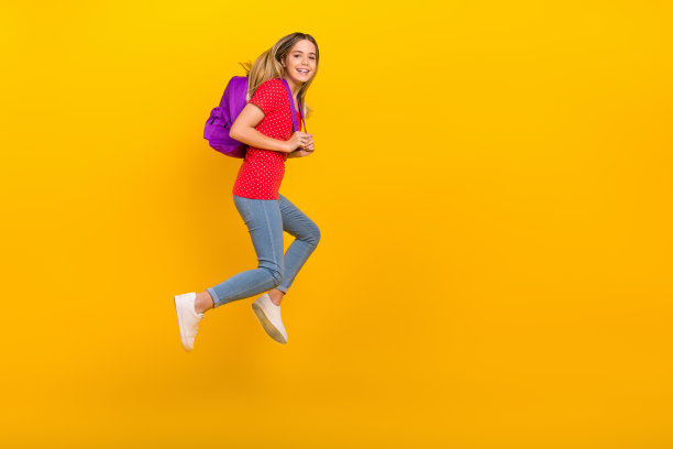 年轻活力女孩全身侧面照片，跑步时手持包，背景为黄色。图片下载