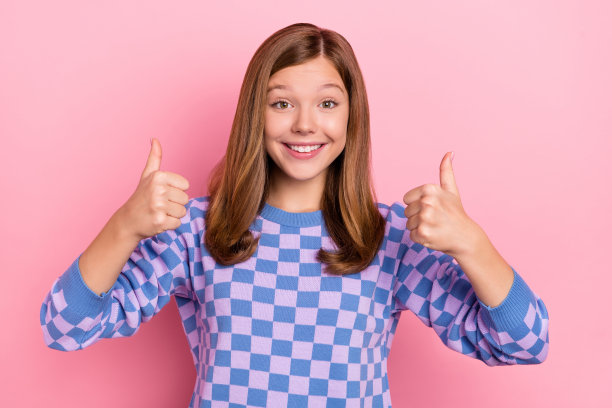 穿着格子毛衣的棕色乐观酷女孩在粉色背景下竖起大拇指的照片图片下载