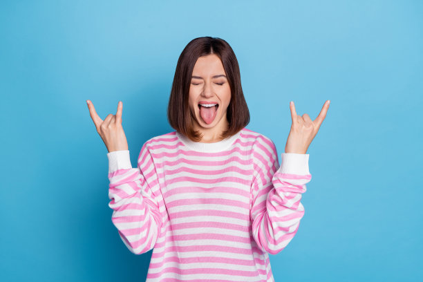 穿着毛衣的酷炫年轻棕发女士在蓝色背景下做出摇滚手势的照片图片下载