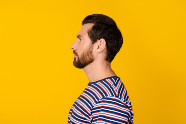 自信男士侧面照片，留着时尚胡须，穿着条纹衬衫，注视着空白的标志，背景为黄色。图片下载
