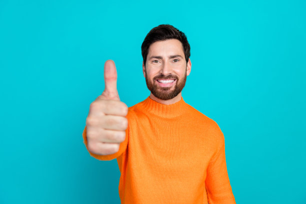 穿着橙色时尚服装、满意的帅气男士在青色背景下竖起大拇指的照片图片下载