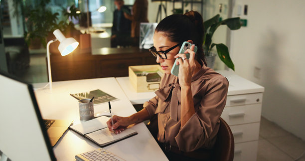 电话会议，写笔记的女商人在办公室为客户预约、安排或预定，夜间进行。手机、书籍或秘书在沟通、计划，接待员加班倾听。图片下载