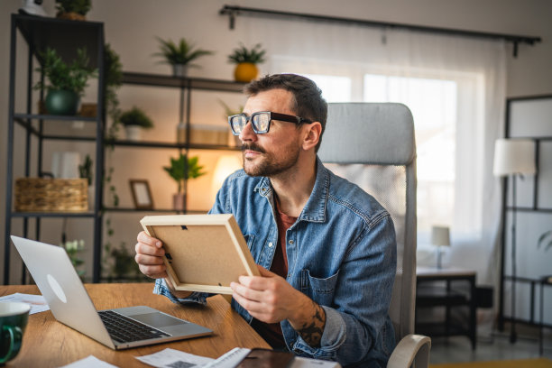 怀旧的男人在家办公，凝视着相框中的照片。图片下载