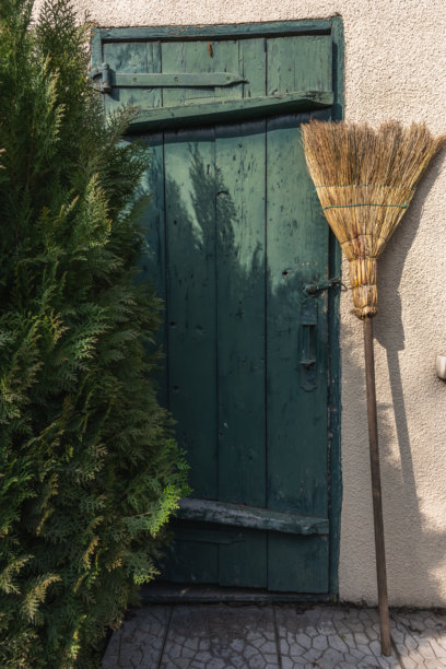 花园扫帚靠在老谷仓的墙上，周围是柏树，竖版照片。春季花园清理工作的季节性场景。图片下载