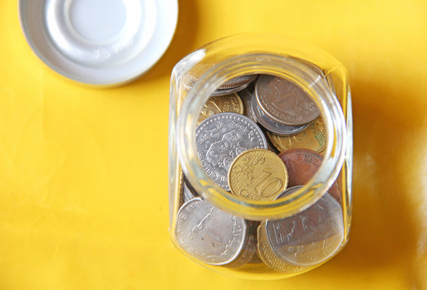 玻璃罐中装有硬币和美元，背景为黄色。为紧急情况储蓄。这张照片可以用作金融背景。图片下载