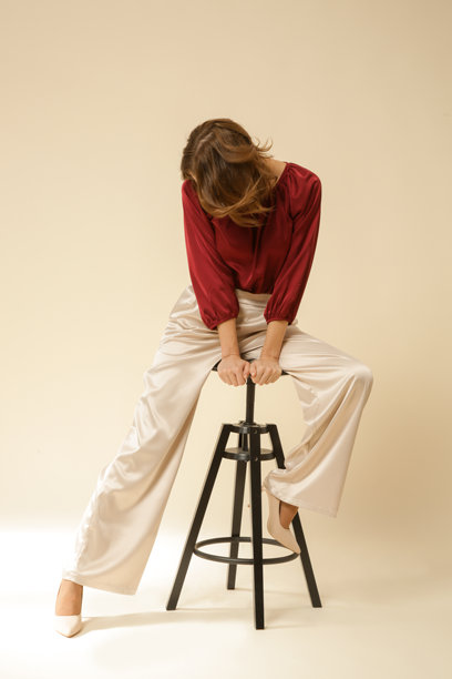 一系列年轻女性模特在摄影棚中穿着简单的丝绸缎美丽服装，酒红色上衣和米色宽腿裤的照片。图片下载