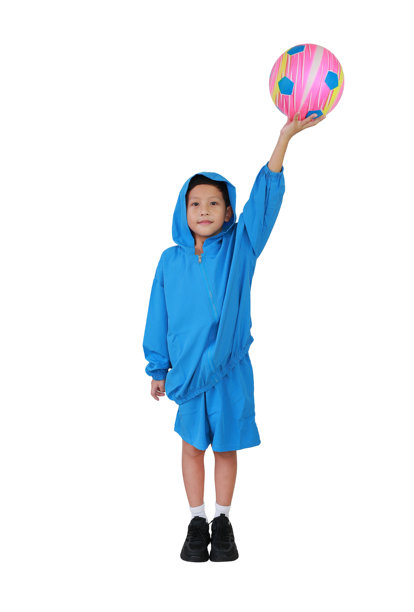 穿着蓝色帽衫或运动服的亚洲小男孩站着，手里拿着足球，背景为白色。全身照片，带有抠图。图片下载