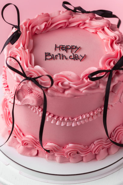 精致的兰贝斯风格生日蛋糕，配有粉色奶油奶酪糖霜，顶部装饰有复古风格的奶油花纹和“生日快乐”字样。粉色背景。图片下载