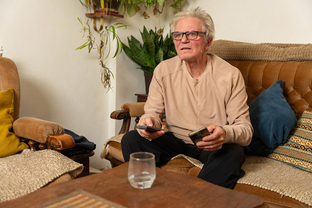 老年男子在家沙发上看电视并使用智能手机图片下载
