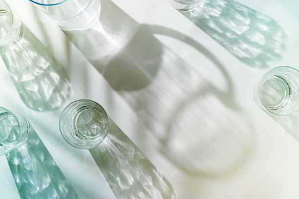 透明水杯和水壶在阳光下的棕榈叶阴影下，白色背景，柔和色调的极简风格照片，俯视角度，闪亮的杯子在自然光下闪烁，夏季饮品。图片下载