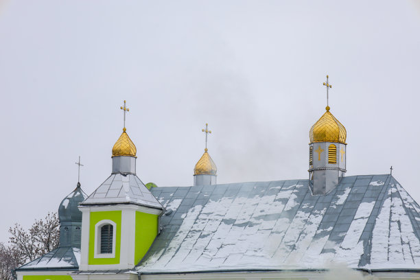 这张照片展示了一座金色圆顶的教堂，背景是灰色的冬季天空。教堂的墙壁是浅色的，带有绿色装饰，灰色的屋顶上覆盖着雪。图片下载