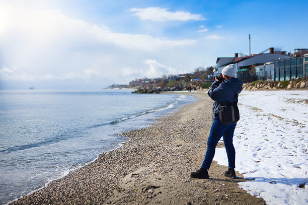 冬季海岸边戴着贝雷帽的女性摄影师拍摄照片。图片下载