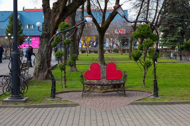 乌克兰桑比尔 - 2025年3月12日：照片展示了一张形状如两个心形的长椅，位于公园内。长椅的靠背是红色心形，底座为金属材质，带有装饰元素。图片下载