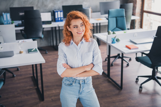 高角度视图照片，成功的年轻女商人双臂交叉，沉思于现代阁楼风格的室内办公室。图片下载