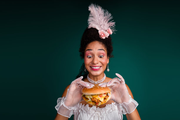 高贵女士渴望吃垃圾汉堡的照片，现代与过去生活方式的对比，背景为绿色。图片下载